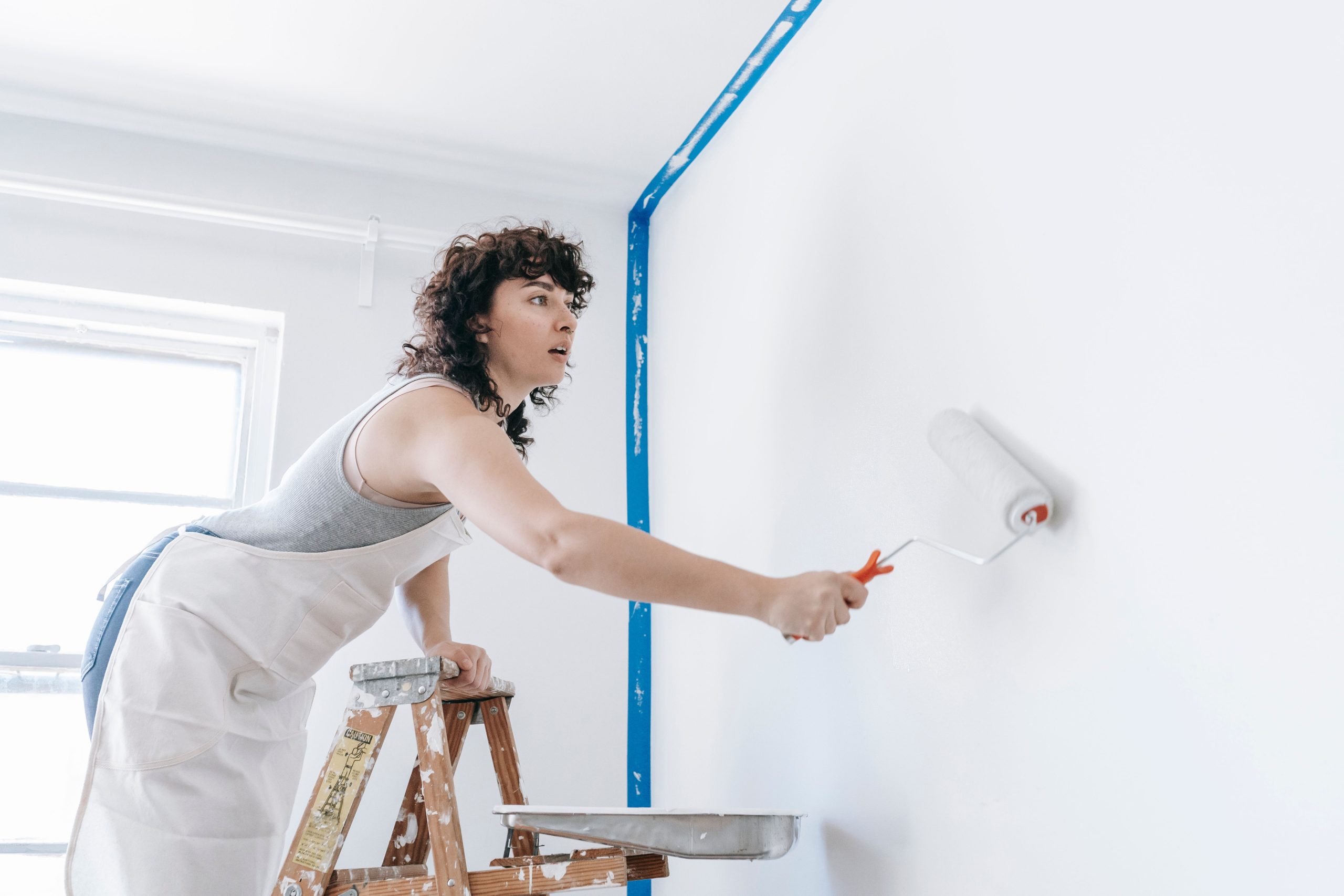 Femme sur une échelle peignant un mur blanc